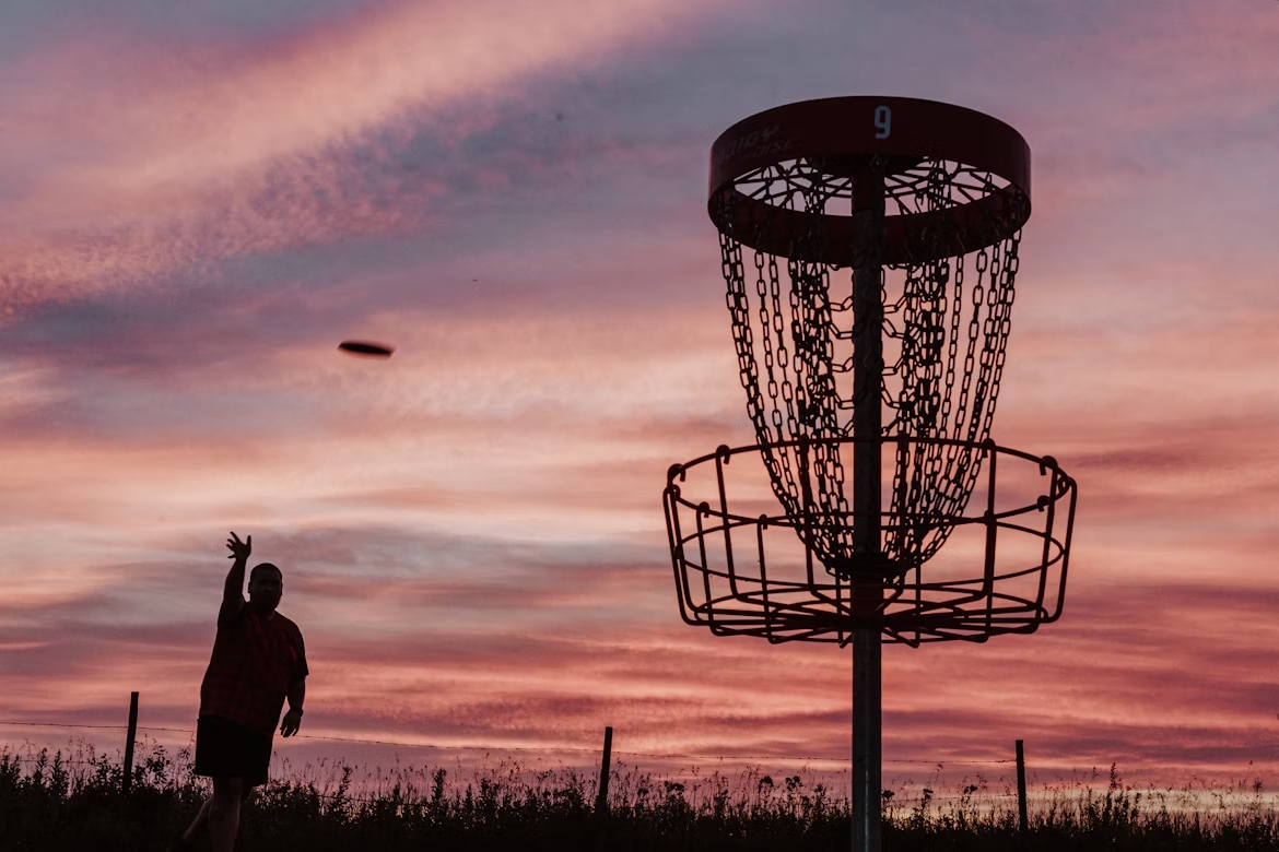 pole disc golf jitsa o zachodzie. gracz disc golf rzucający do kosza.